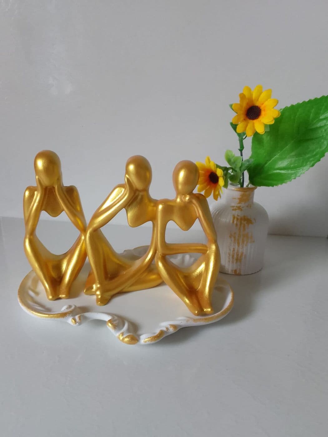 Trío de figuras decorativas con acabado dorado sobre una bandeja blanca con filo dorado