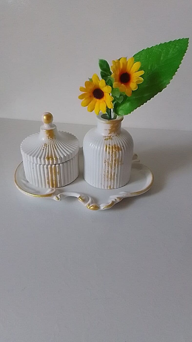 Joyero y florero blancos con detalles dorados sobre bandeja, con girasoles
