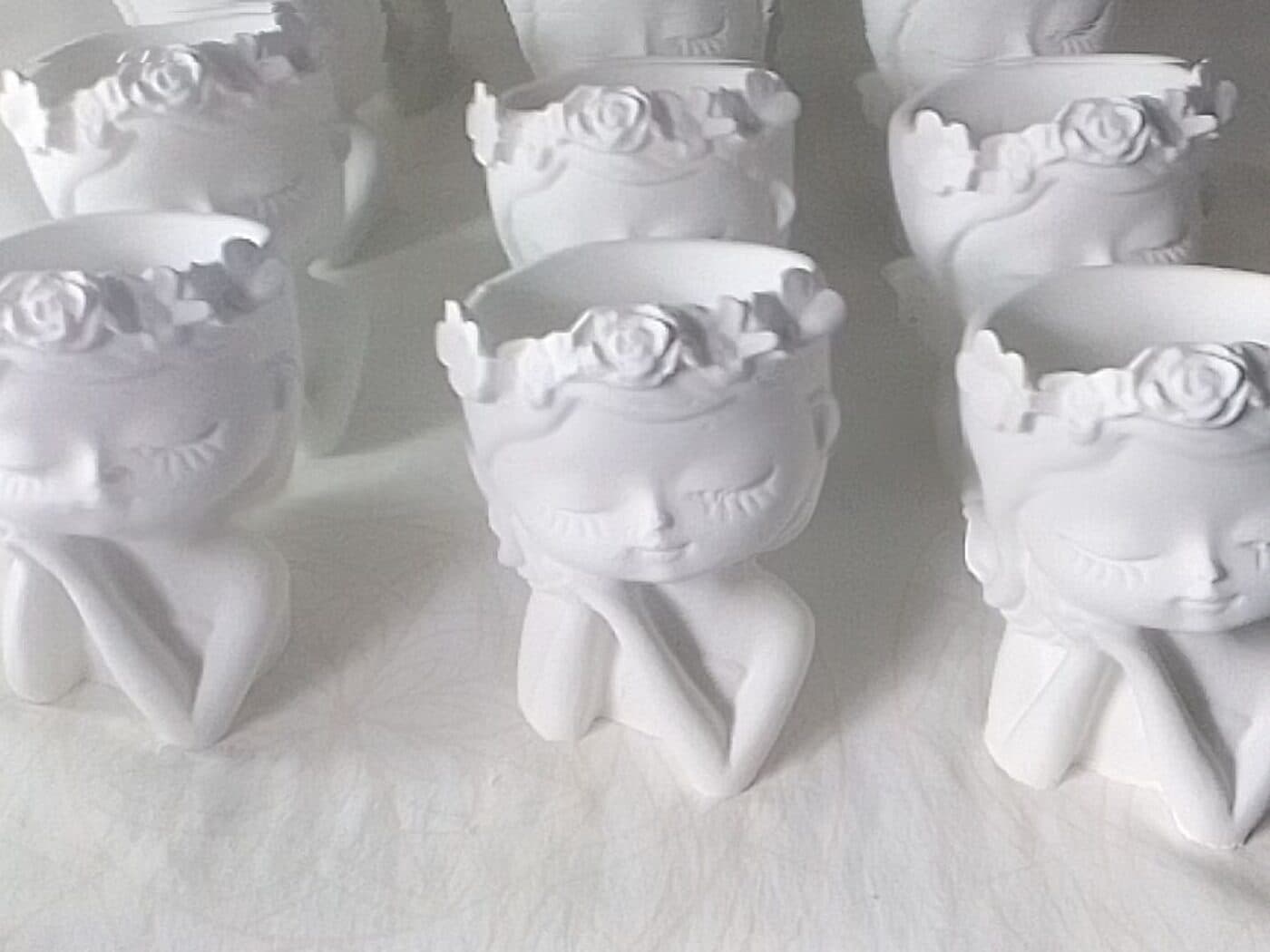Materas de cemento blanco con forma de muñeca y corona de flores